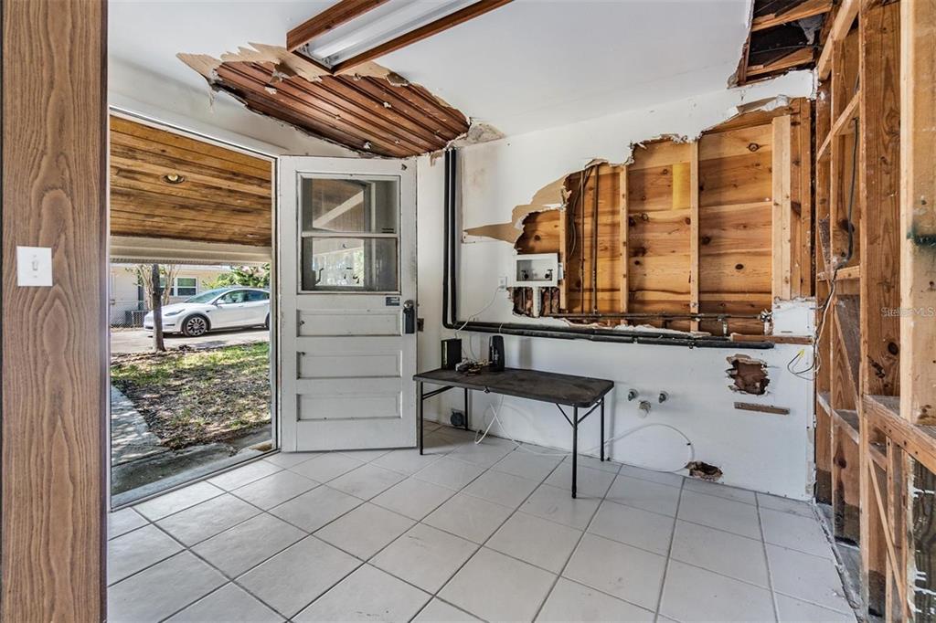An unfinished room with exposed wall studs, damaged ceiling panels, tiled flooring, and an exterior door — 2620 TRENT ROAD, PALM HARBOR, FL