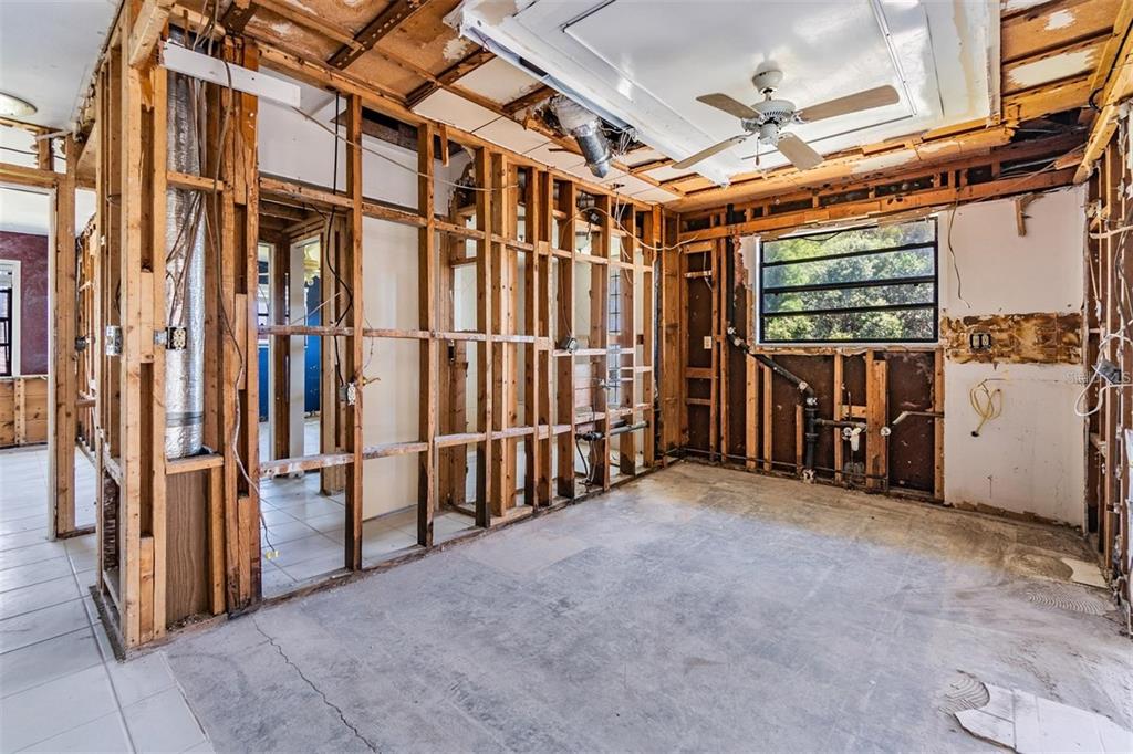 An interior room under renovation with exposed wood wall studs, concrete flooring, and a ceiling fan — 2620 TRENT ROAD, PALM HARBOR, FL
