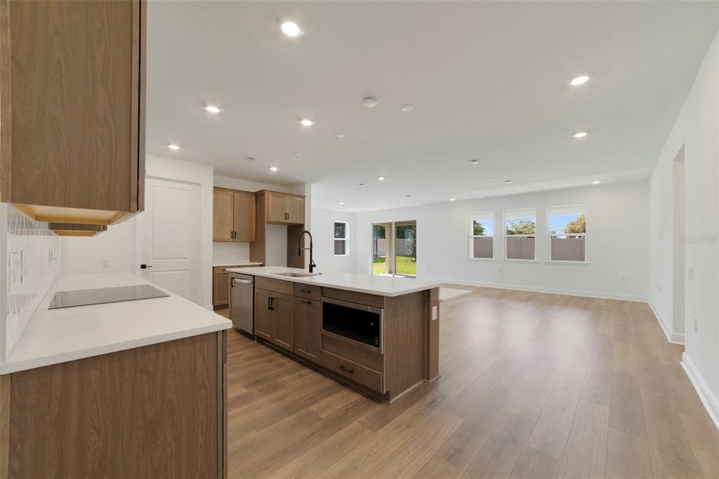A modern kitchen with wood cabinets and a white island opens into a spacious living area — 3004 WATER CLOVER COURT, APOPKA, FL