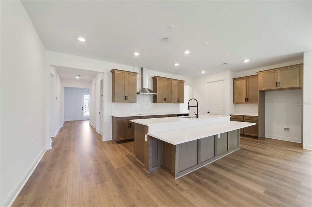 A modern kitchen features wood cabinets, a white quartz island, and light wood-look flooring — 3004 WATER CLOVER COURT, APOPKA, FL