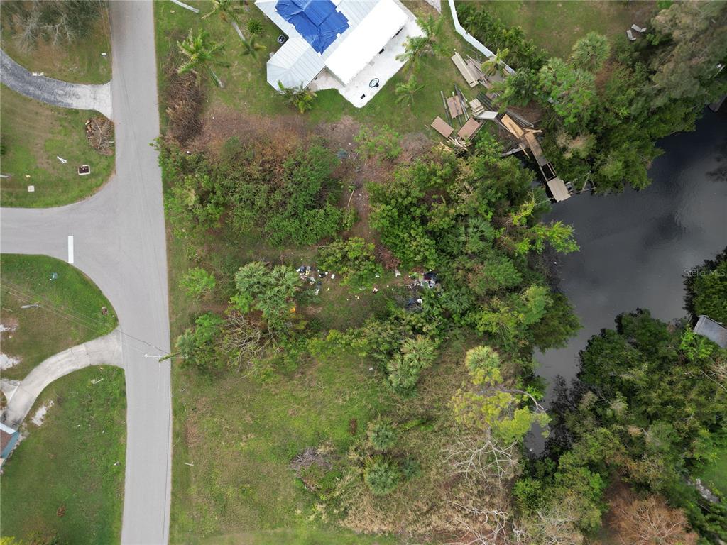 An aerial view shows a vacant, wooded lot situated between a road and a canal — 108 BARRE DRIVE NW, PORT CHARLOTTE, FL