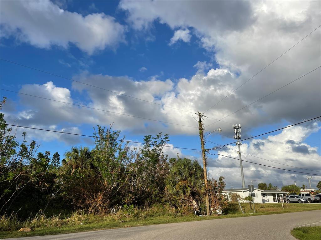 A view of a vacant, overgrown lot with a utility pole and nearby houses — 108 BARRE DRIVE NW, PORT CHARLOTTE, FL
