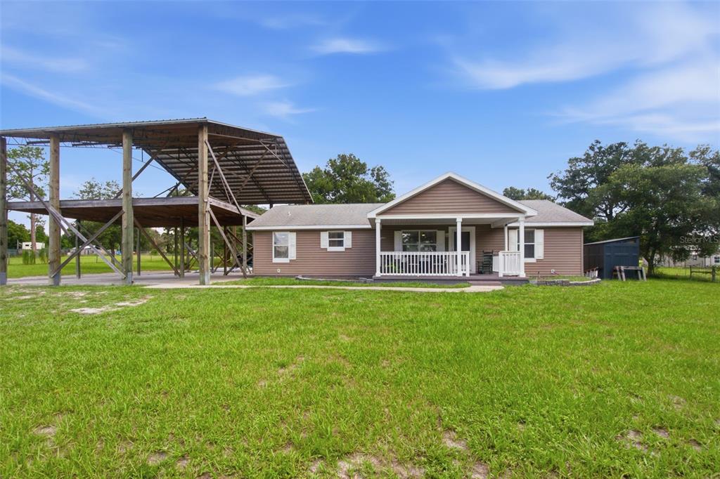 A single-story house with tan siding and a large attached metal carport on a lawn — 32416 PINE ROAD, EUSTIS, FL