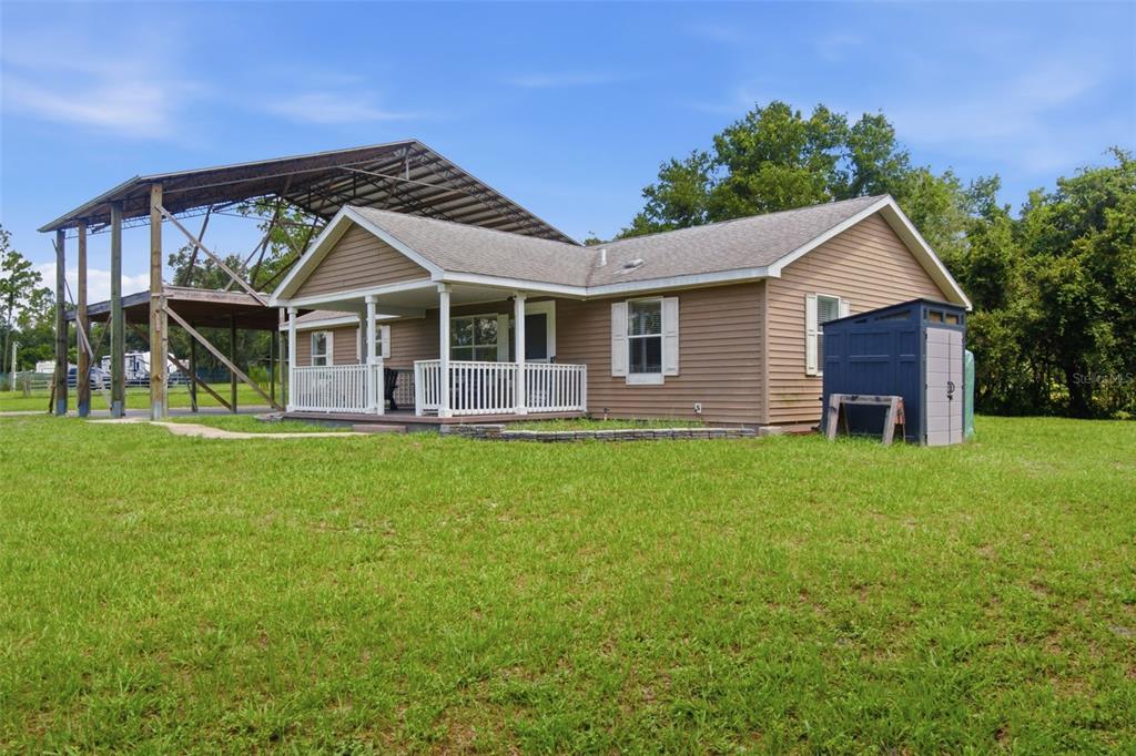 A tan house with a front porch and an attached metal carport sits on grass — 32416 PINE ROAD, EUSTIS, FL
