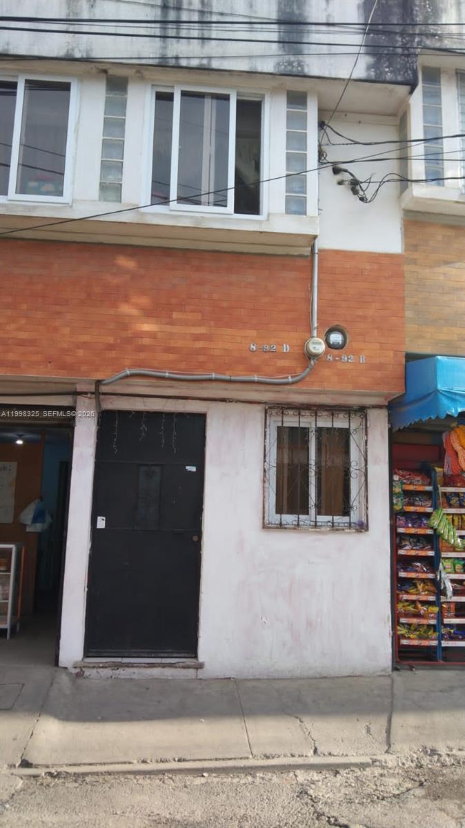 A two-story building exterior features a brick facade, a black door, and a ground-floor window — 9 Calle 8-92 Zona 11, MA 01057, MA