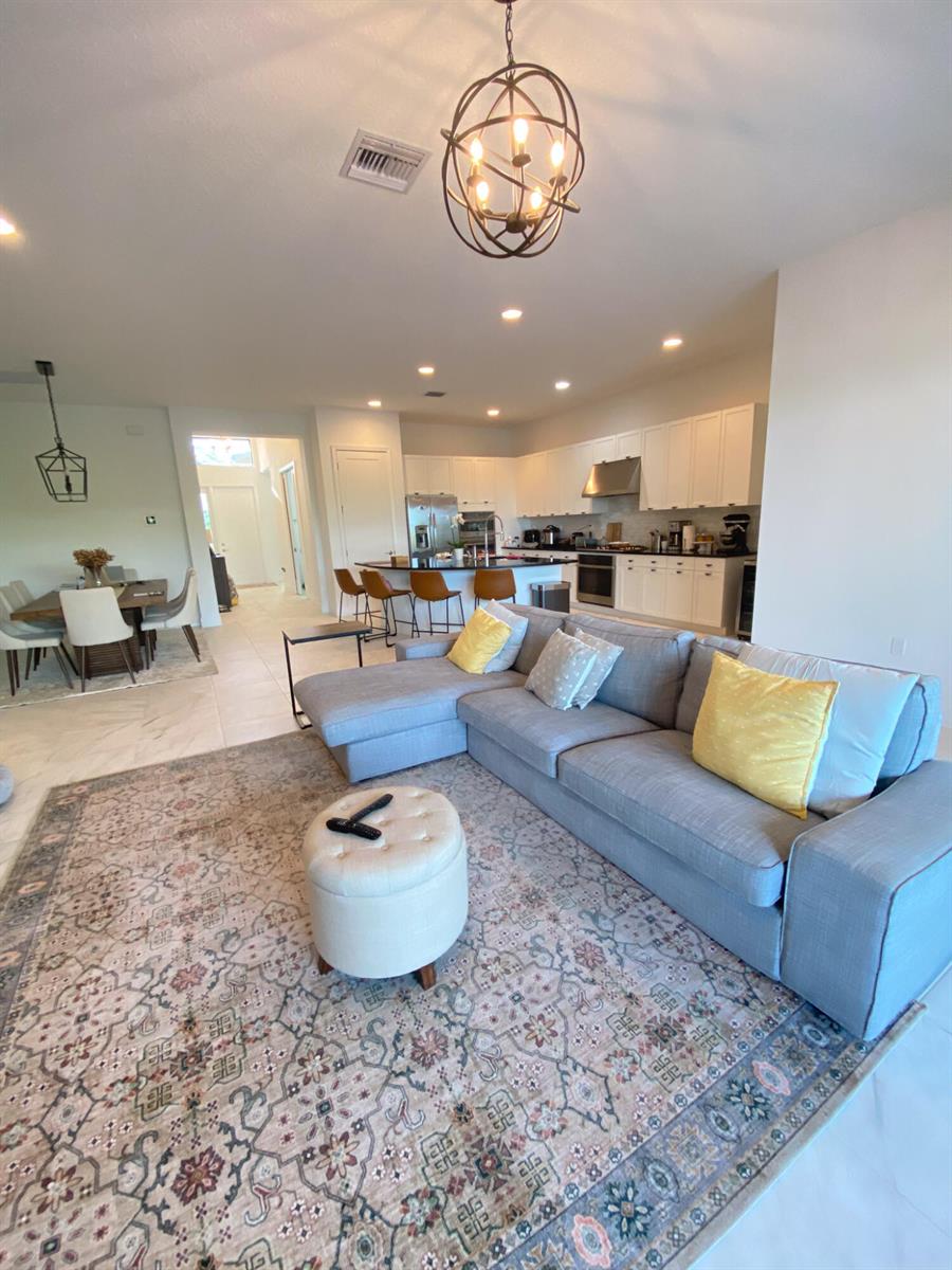 An open-concept living room features a grey sectional sofa, patterned rug, and adjacent kitchen area — 17296 Sea Blossom Way, Boca Raton FL 33496, BOCA RATON, FL