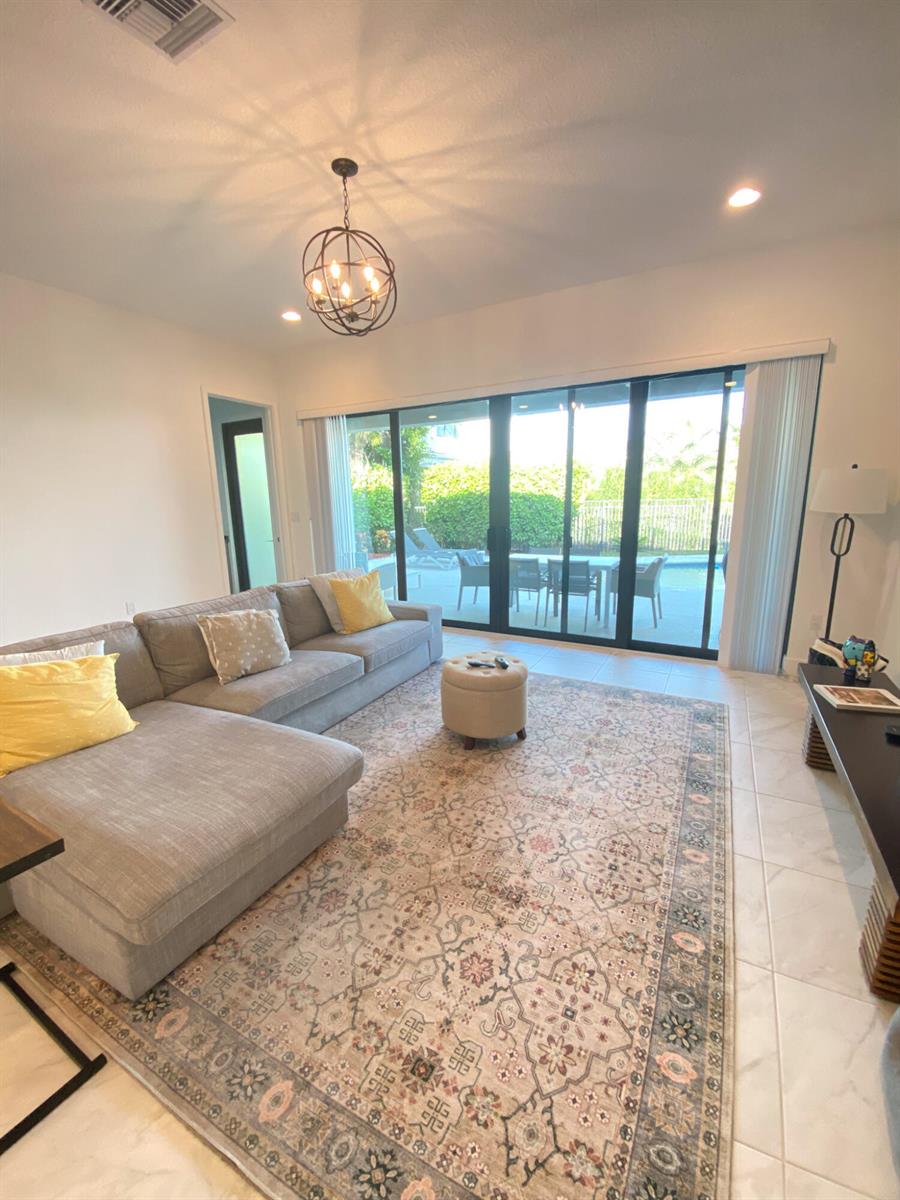 A living room features a grey sectional sofa, a patterned area rug, and large sliding doors — 17296 Sea Blossom Way, Boca Raton FL 33496, BOCA RATON, FL
