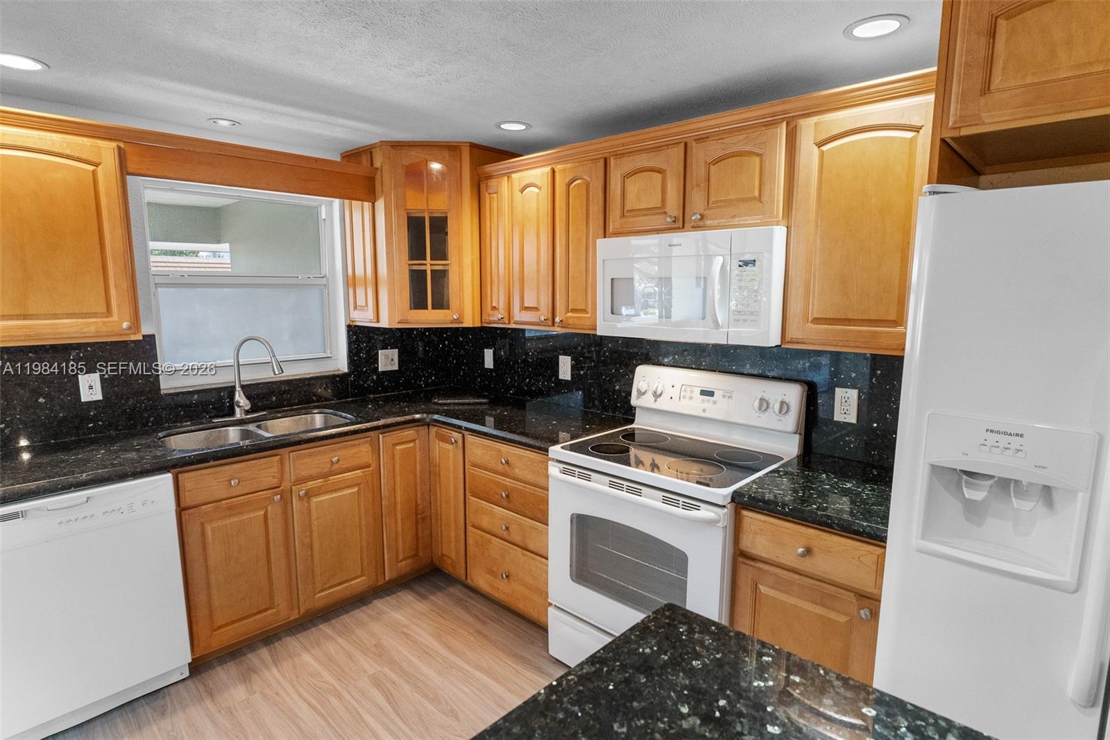 A kitchen features oak cabinets, black granite countertops, white appliances, and light wood-look flooring — 1340 NE 28th Ave # 244, Pompano Beach FL 33062, POMPANO BEACH, FL