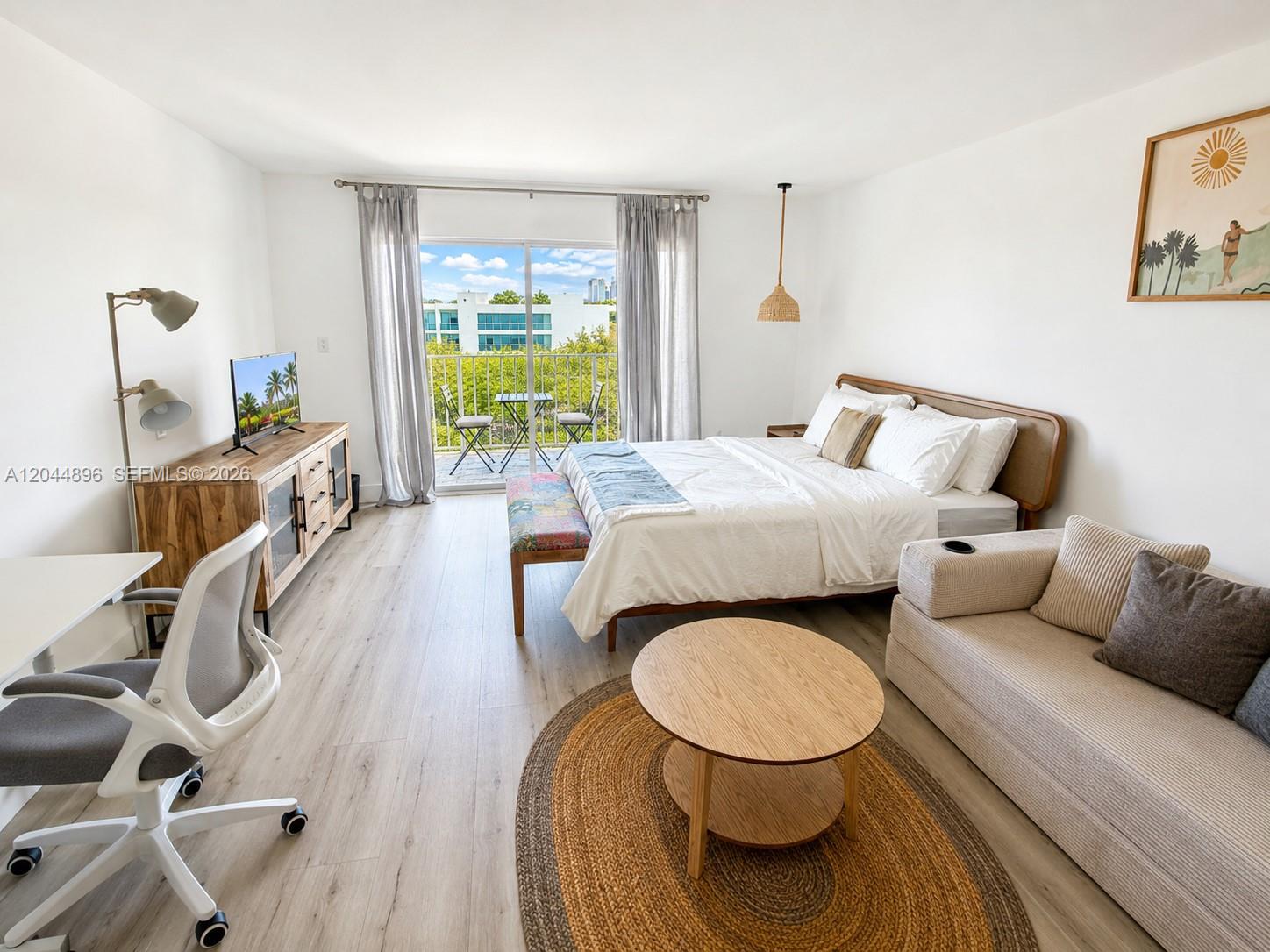 A bedroom features a bed, a small sofa, a desk, and a balcony with outdoor seating — 650 NE 64 ST # G506, Miami FL 33138, MIAMI, FL