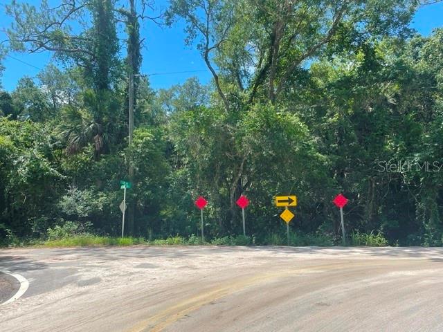 A paved road curves in front of a wooded lot with several traffic signs — 2075 COUNTRY ROAD 75, BUNNELL, FL