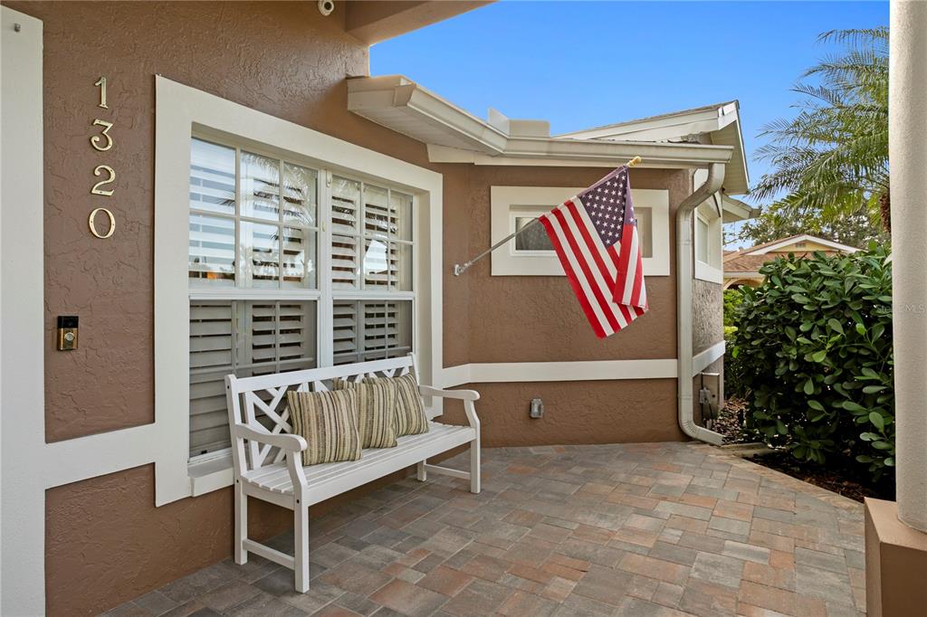 A covered patio with a white bench, an American flag, and a window with shutters — 1320 52ND AVENUE NE, ST PETERSBURG, FL