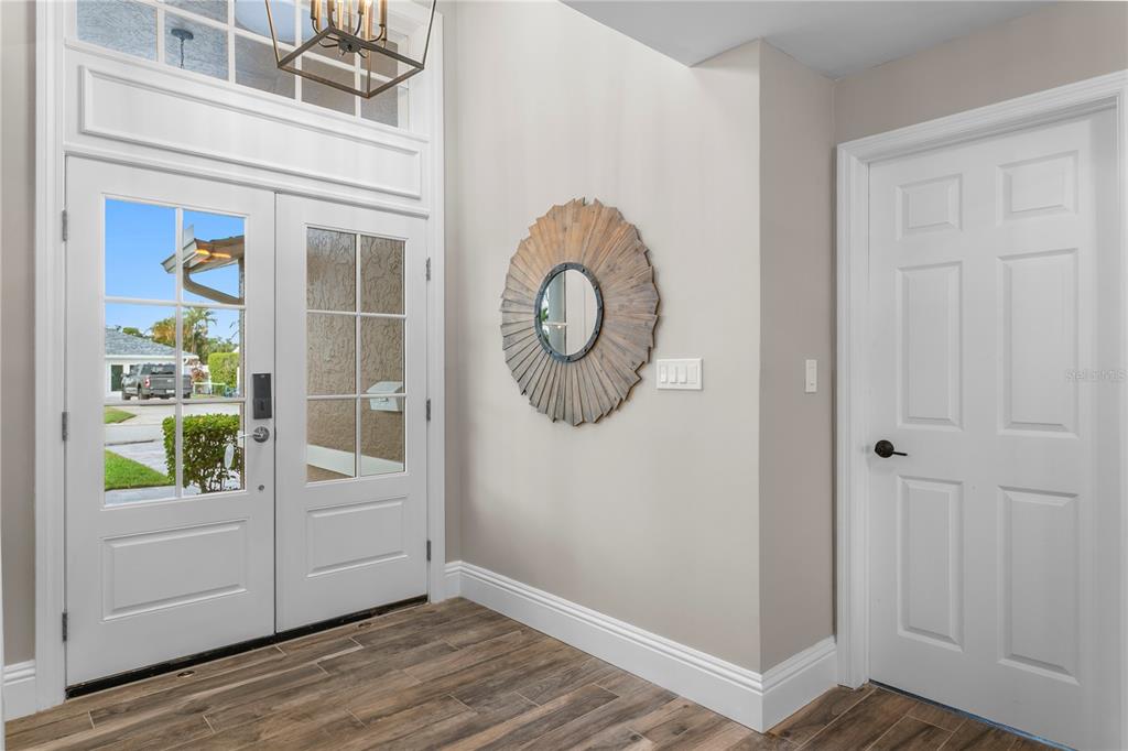 A bright entryway features a white double door, wood-look tile flooring, and a round mirror — 1320 52ND AVENUE NE, ST PETERSBURG, FL