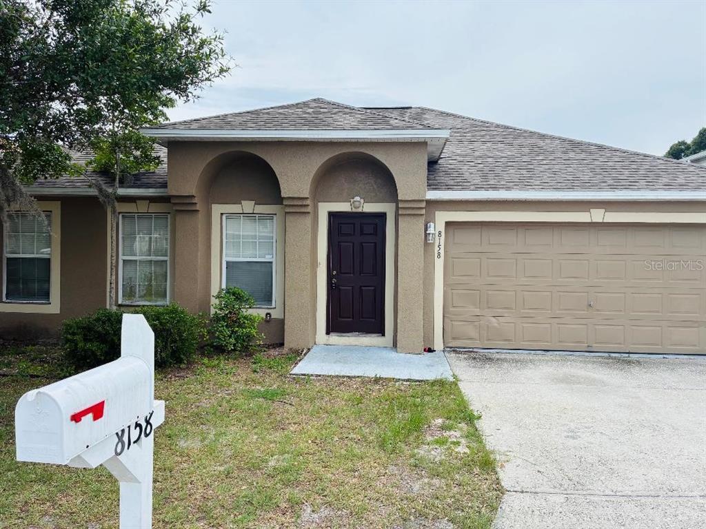 A single-story house with a tan stucco exterior, a dark front door, and a two-car garage — 8158 SETTLERS CREEK CIRCLE, LAKELAND, FL