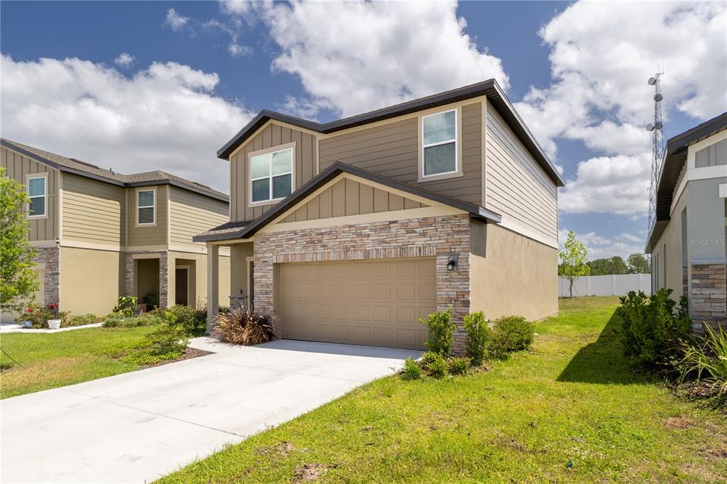 A two-story house with a stone-accented garage, tan siding, and a concrete driveway — 8688 SPORTSMAN LOOP, GROVELAND, FL