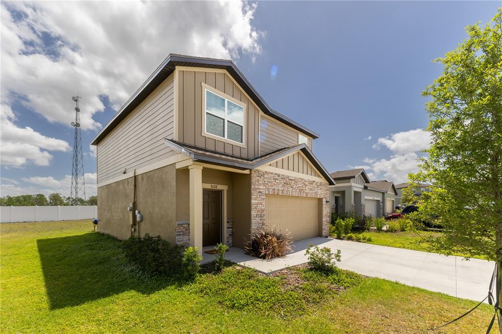 A two-story suburban house features a tan stucco and siding exterior with a stone-accented garage — 8688 SPORTSMAN LOOP, GROVELAND, FL