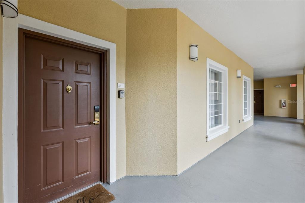 A brown front door with a keypad lock sits on a covered outdoor apartment walkway — 8774 WORLDQUEST BOULEVARD UNIT 7204, ORLANDO, FL