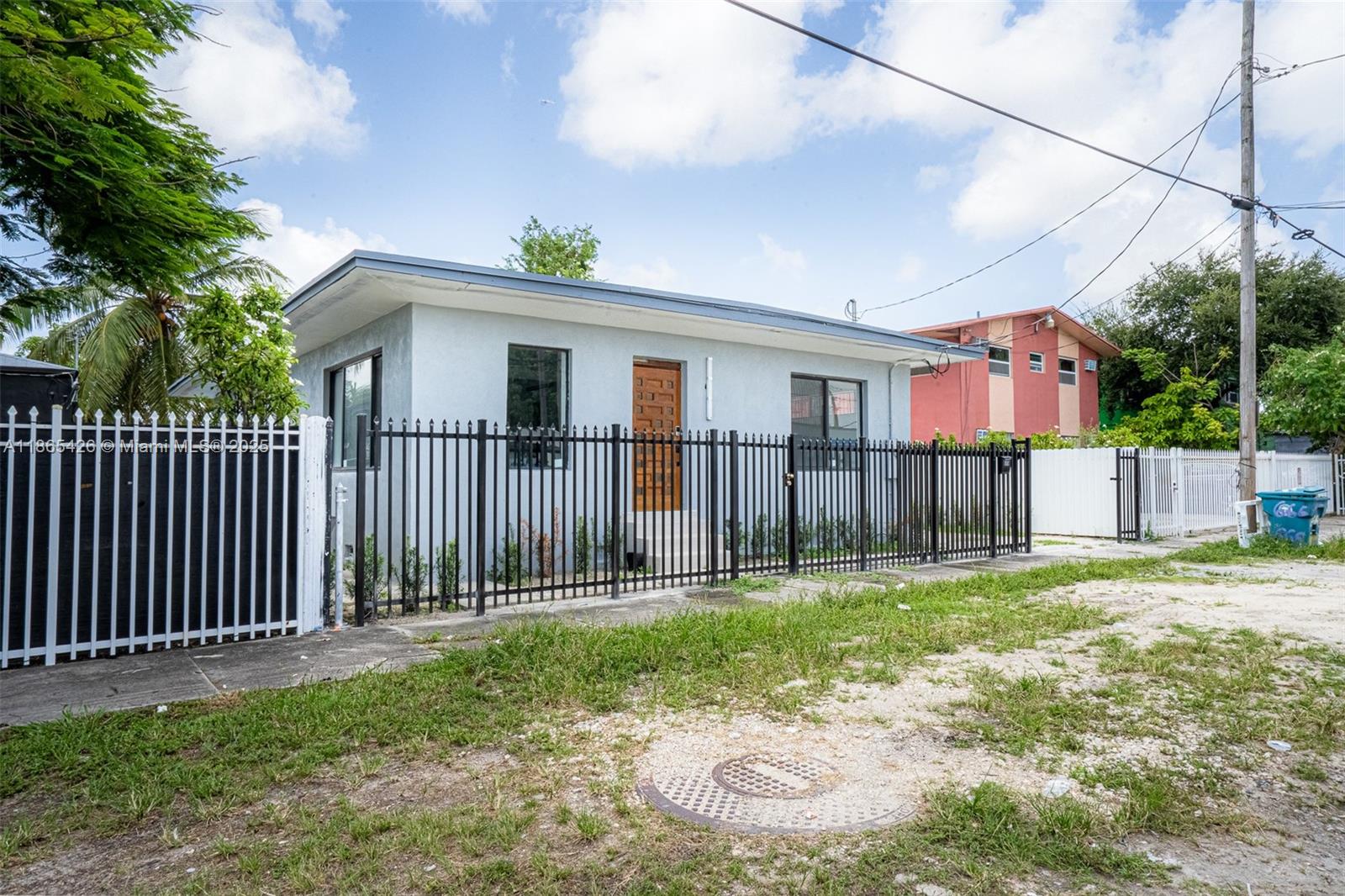 A single-story light blue house with a wooden door sits behind a black metal fence — 666 NW 28th St, Miami FL 33127, MIAMI, FL