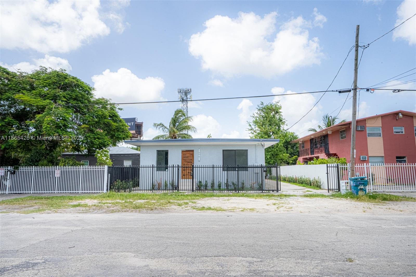 A single-story light-colored house sits behind a black metal fence under a blue sky — 666 NW 28th St, Miami FL 33127, MIAMI, FL