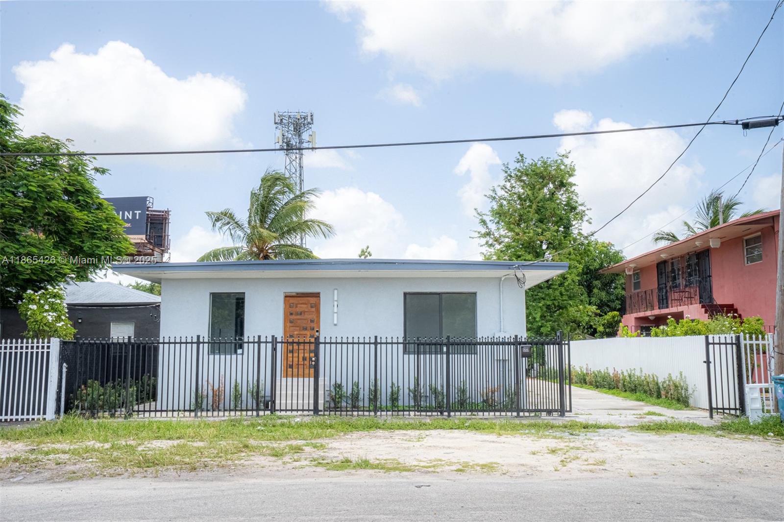 A single-story light-colored house with a wooden door sits behind a black metal fence — 666 NW 28th St, Miami FL 33127, MIAMI, FL