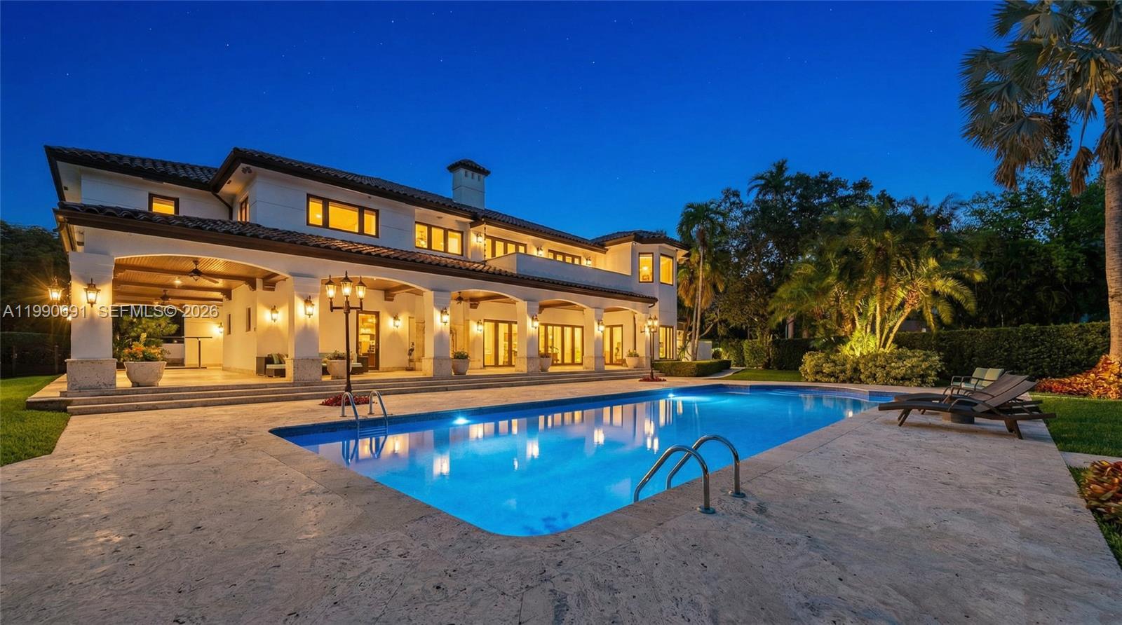 A two-story Mediterranean-style house features a large swimming pool and a covered patio at night — 7701 Old Cutler Rd, Coral Gables FL 33143, CORAL GABLES, FL