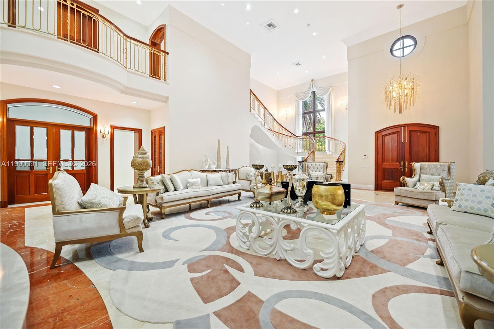 A grand, high-ceilinged living room features a curved staircase, marble flooring, and ornate furniture — 7701 Old Cutler Rd, Coral Gables FL 33143, CORAL GABLES, FL