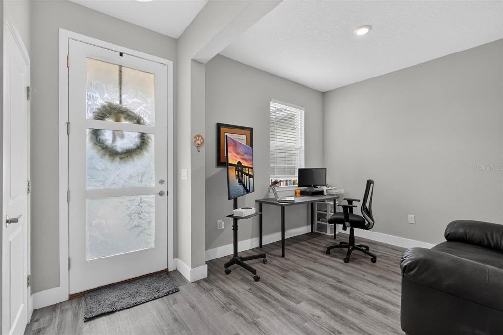 A home office with gray walls, wood-look flooring, a desk, and a front entry door — 20 PICKCANE LANE, PALM COAST, FL