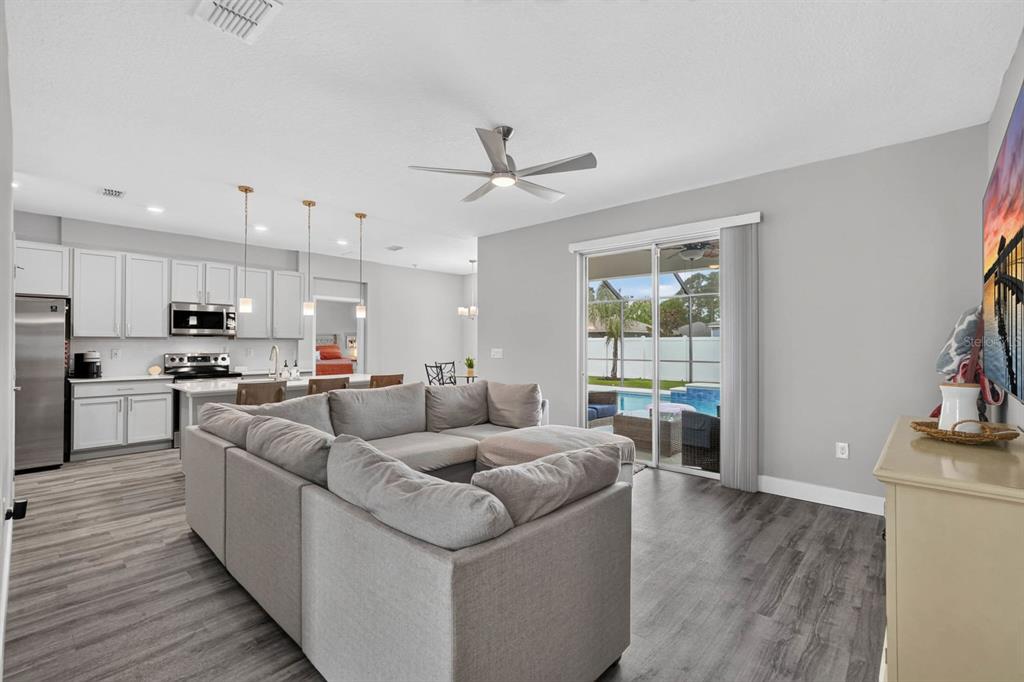 A living room with a gray sectional sofa opens to a kitchen and a backyard pool — 20 PICKCANE LANE, PALM COAST, FL