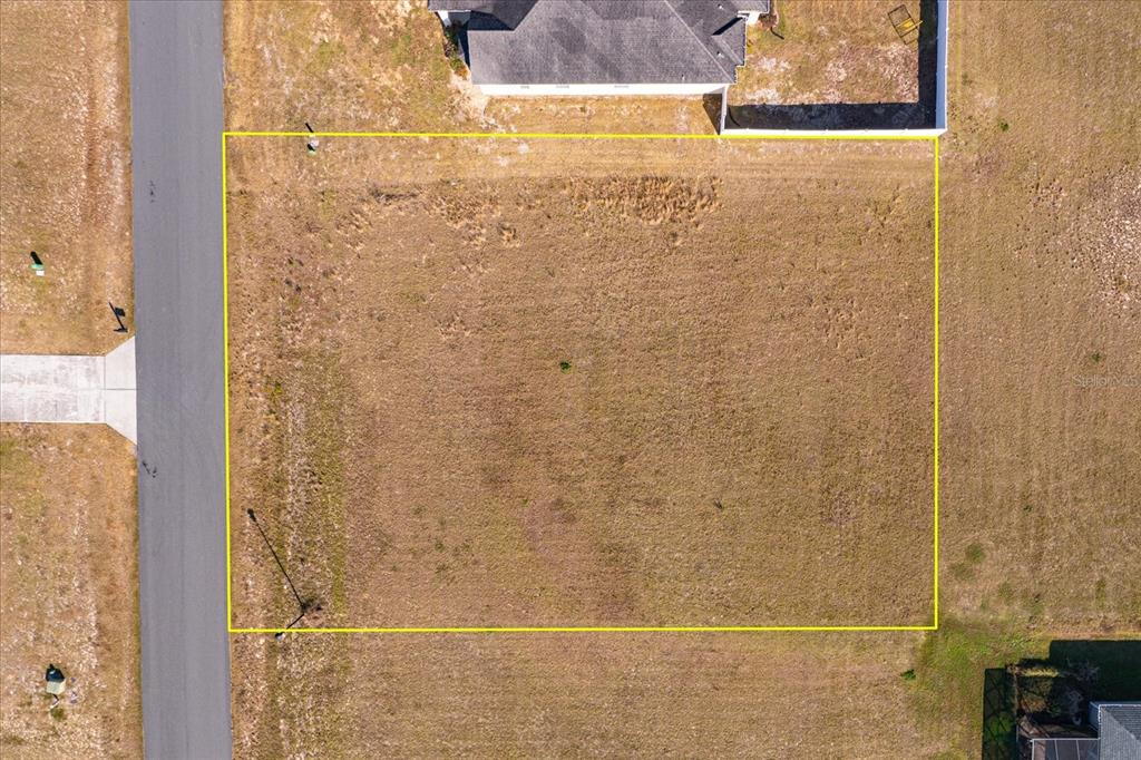 An aerial view shows a vacant, rectangular residential lot outlined in yellow next to a road — 1115 MYRTLE BREEZES COURT, FRUITLAND PARK, FL