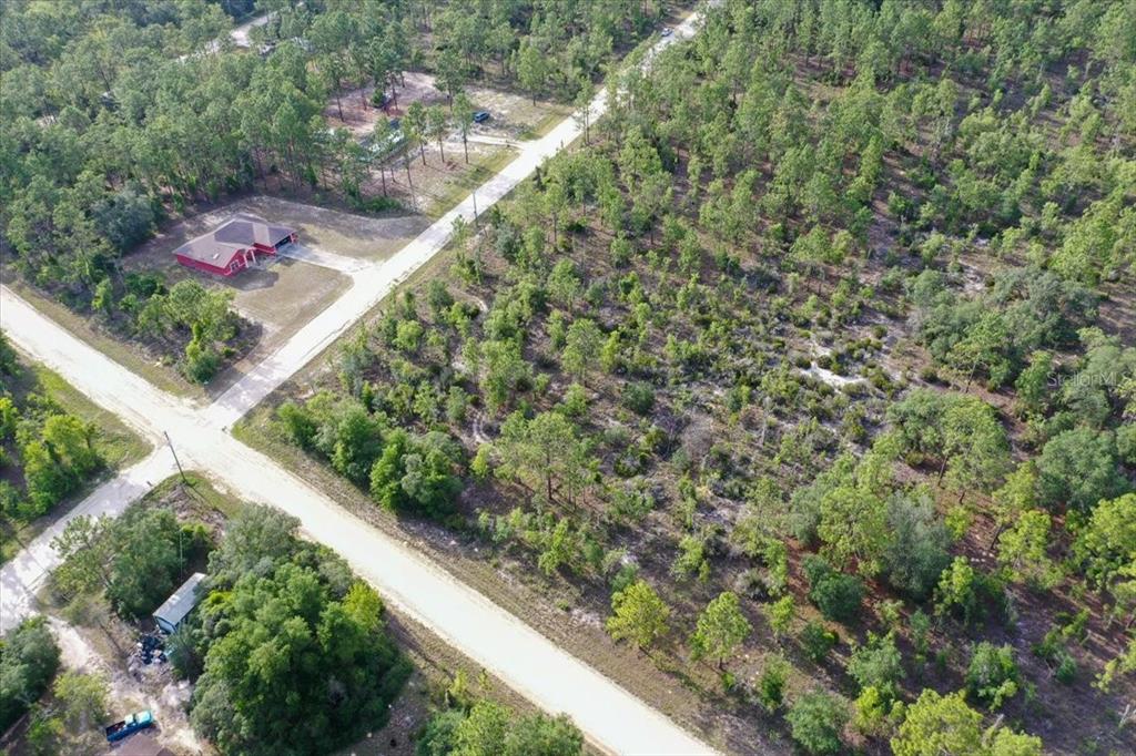 An aerial view shows a dirt road intersecting near a red house and wooded lots — 0000 NE 131 TERRACE LOT 6 TERRACE, WILLISTON, FL