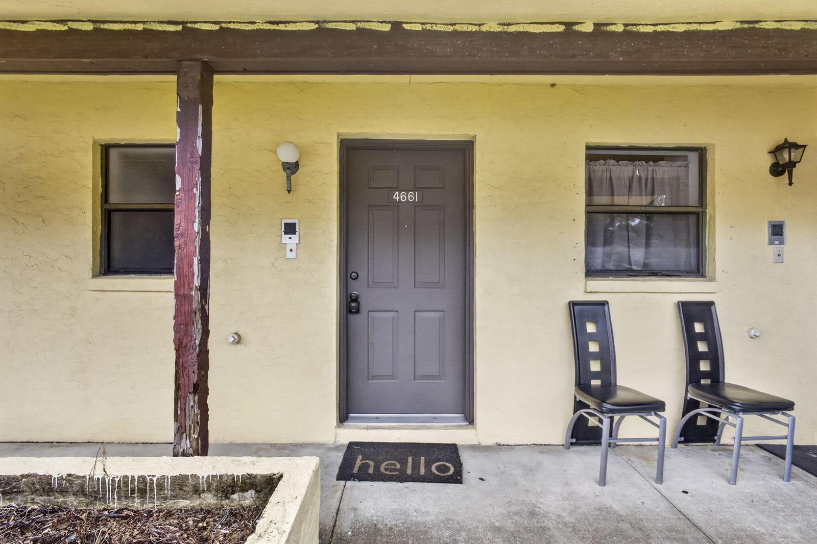 An exterior view of a building entrance with a grey door, two chairs, and windows — 4661 Perth Road # 4661, West Palm Beach FL 33415, WEST PALM BEACH, FL