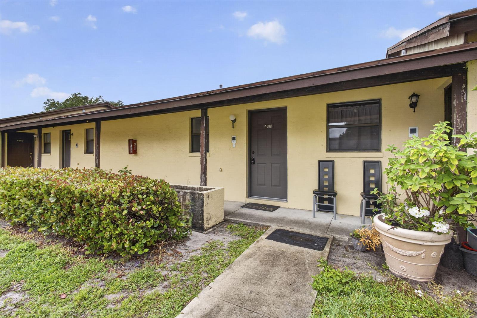 A yellow exterior building features a concrete walkway leading to a brown front door — 4661 Perth Road # 4661, West Palm Beach FL 33415, WEST PALM BEACH, FL