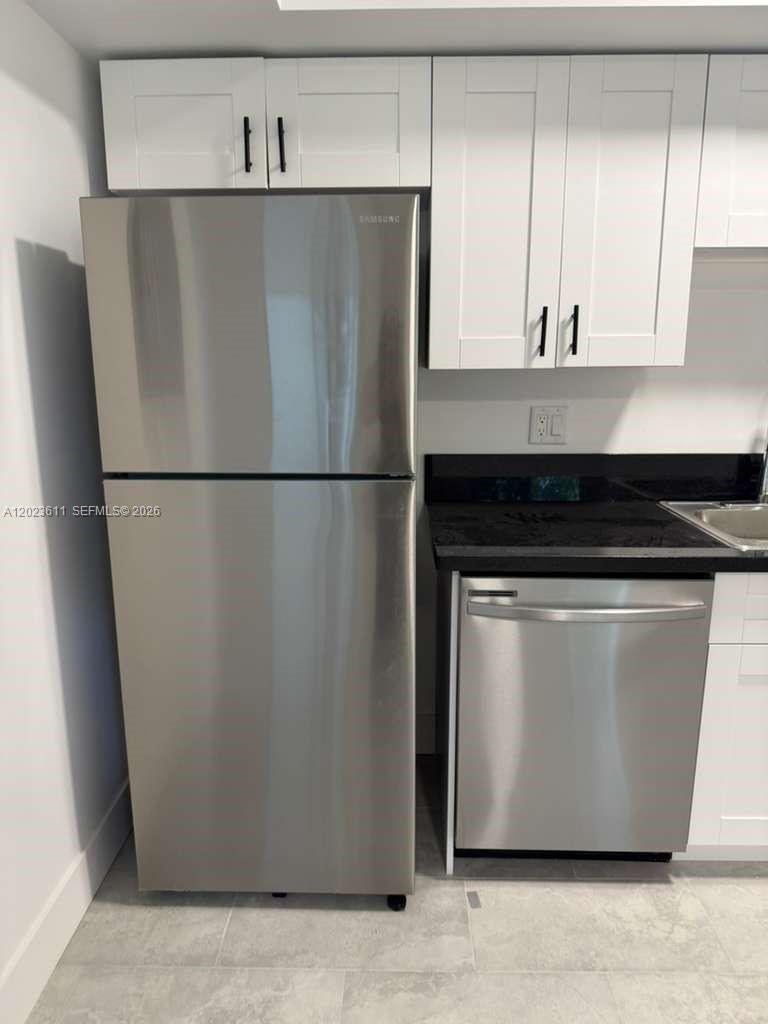 A kitchen features a stainless steel refrigerator, a dishwasher, and white cabinets with black hardware — 147 Nw 59th St # 204, Miami FL 33127, MIAMI, FL