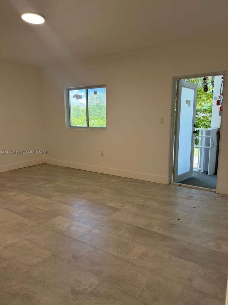 An empty room features light-colored tile flooring, white walls, a window, and an open door — 147 Nw 59th St # 204, Miami FL 33127, MIAMI, FL