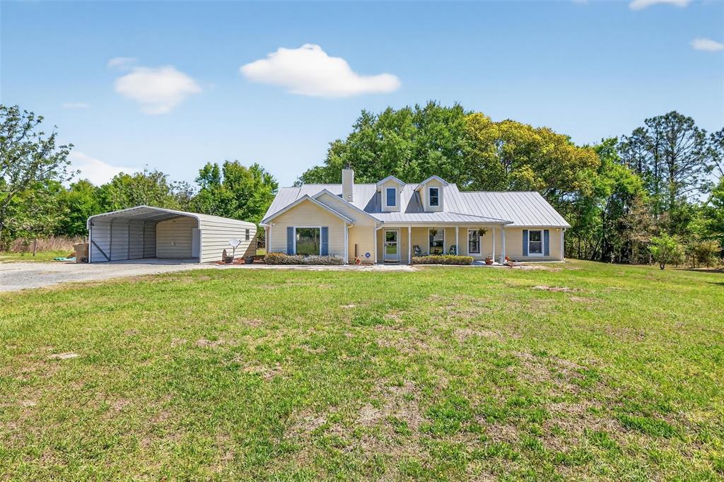 A yellow one-story house with a metal roof and an attached metal carport — 32510 WHITNEY ROAD, LEESBURG, FL