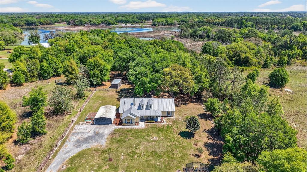 An aerial view shows a house with a metal roof, carport, and shed on acreage — 32510 WHITNEY ROAD, LEESBURG, FL