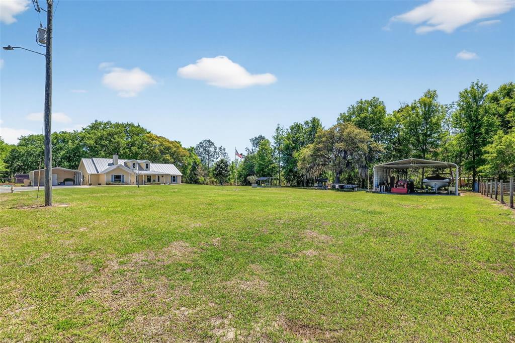 A large grassy yard features a house, a carport with a boat, and trees — 32510 WHITNEY ROAD, LEESBURG, FL