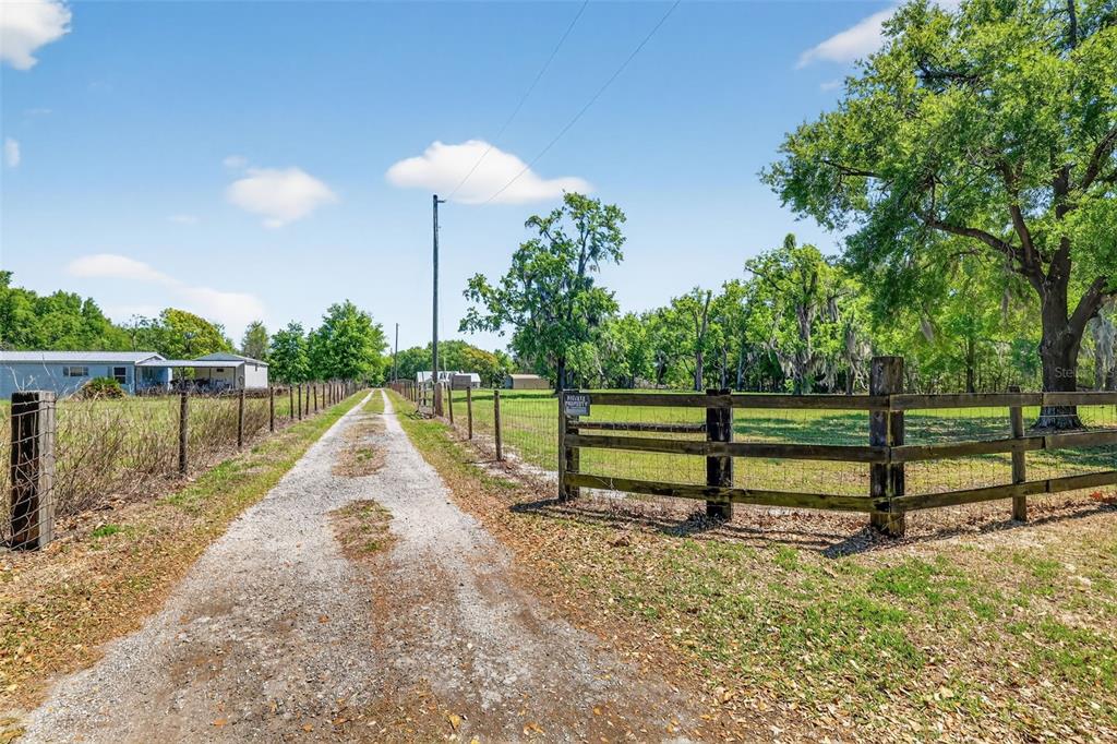 A gravel driveway leads past a wooden fence toward a house on a sunny day — 32510 WHITNEY ROAD, LEESBURG, FL