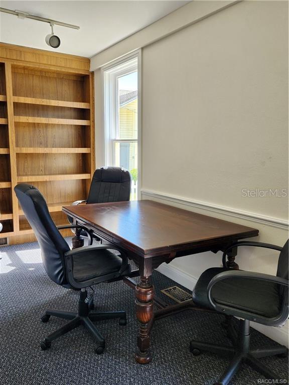 A home office features a wooden desk, three rolling chairs, and built-in wall shelving — 101 S OSCEOLA AVENUE, INVERNESS, FL
