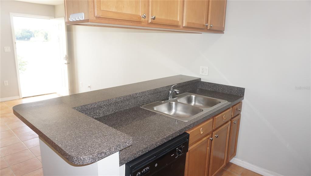A kitchen features wood cabinets, dark speckled countertops, a double-basin sink, and a dishwasher — 220 LAKE PARSONS GREEN UNIT 206, BRANDON, FL