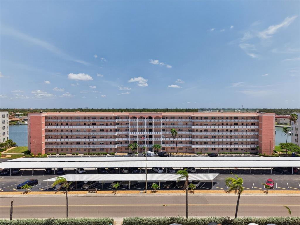 An exterior view of a multi-story pink apartment building with a covered parking lot — 6025 SHORE BOULEVARD S UNIT 602, GULFPORT, FL