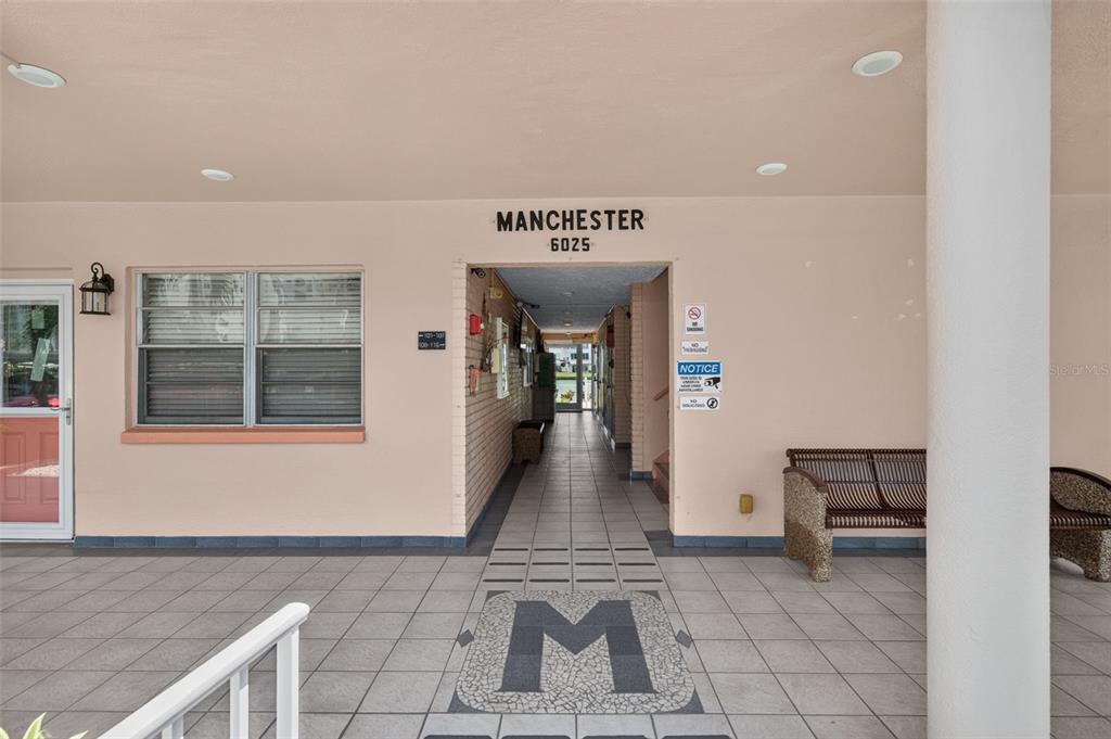 The entrance to a building features a tiled walkway, a large letter M, and benches — 6025 SHORE BOULEVARD S UNIT 602, GULFPORT, FL