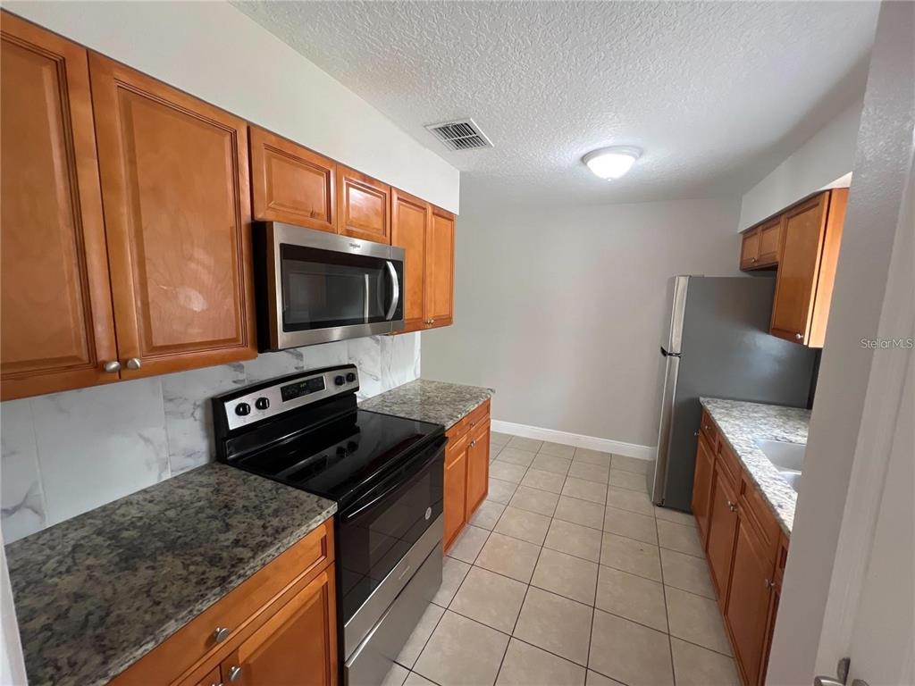 A kitchen features wood cabinets, granite countertops, stainless steel appliances, and light-colored tile flooring — 152 JULIE LANE Unit B, AUBURNDALE, FL