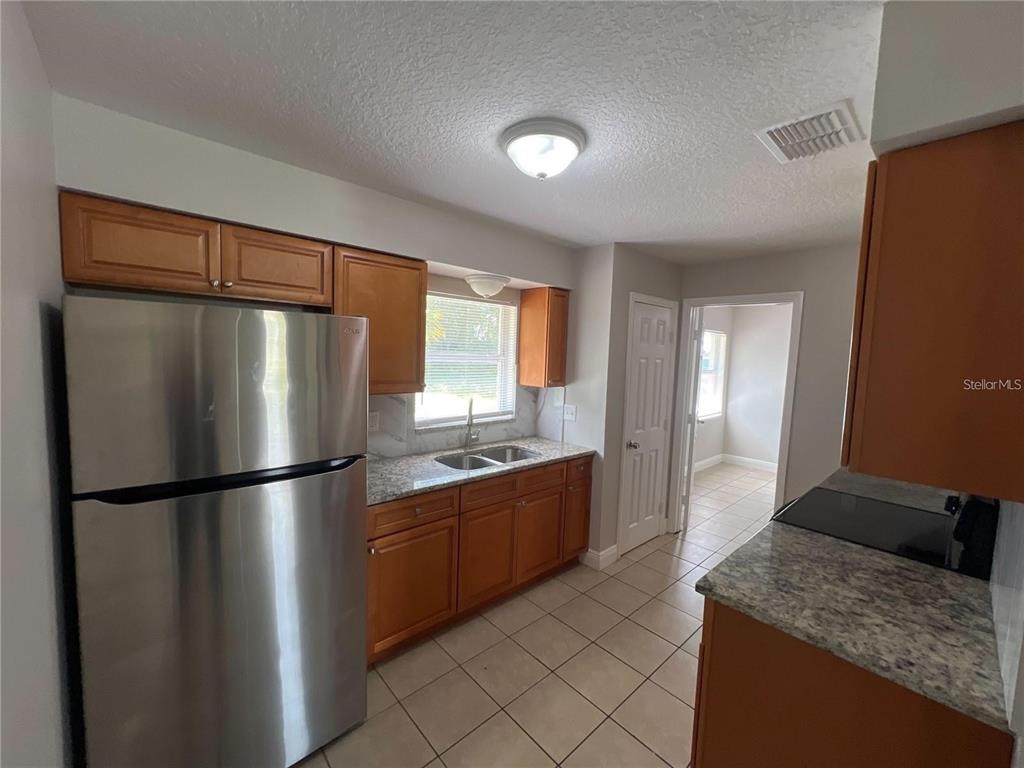 A kitchen features stainless steel appliances, wood cabinets, granite countertops, and light-colored tile flooring — 152 JULIE LANE Unit B, AUBURNDALE, FL