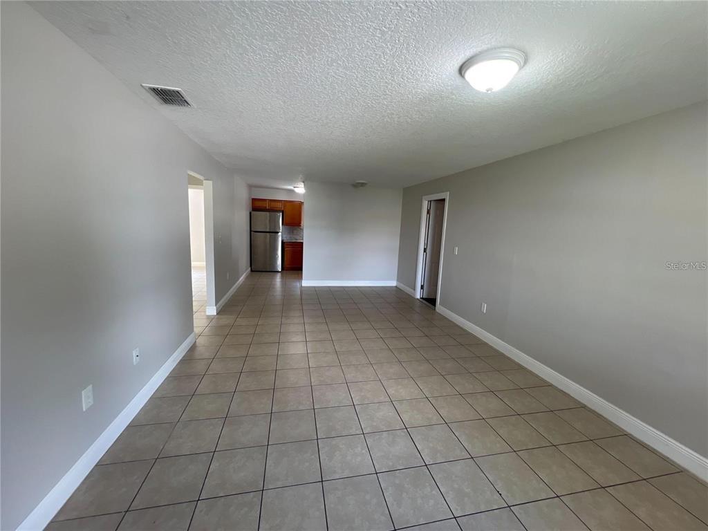 An open-concept room features light gray walls, tile flooring, and a view of the kitchen — 152 JULIE LANE Unit B, AUBURNDALE, FL