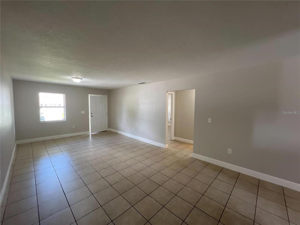 A spacious, empty living room features light-colored tile flooring and neutral gray walls — 152 JULIE LANE Unit B, AUBURNDALE, FL