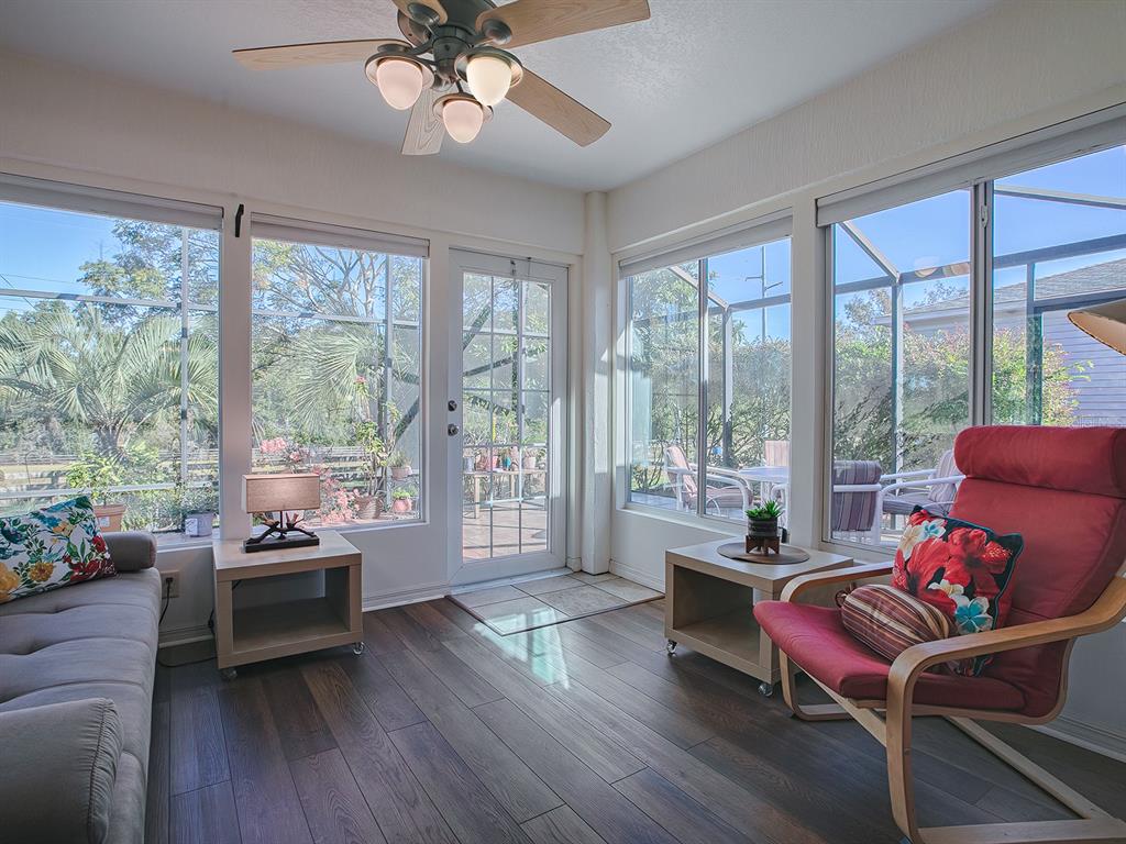 A sunroom features wood-look flooring, a ceiling fan, and large windows overlooking a screened patio — 33236 GRAND CYPRESS WAY, LEESBURG, FL