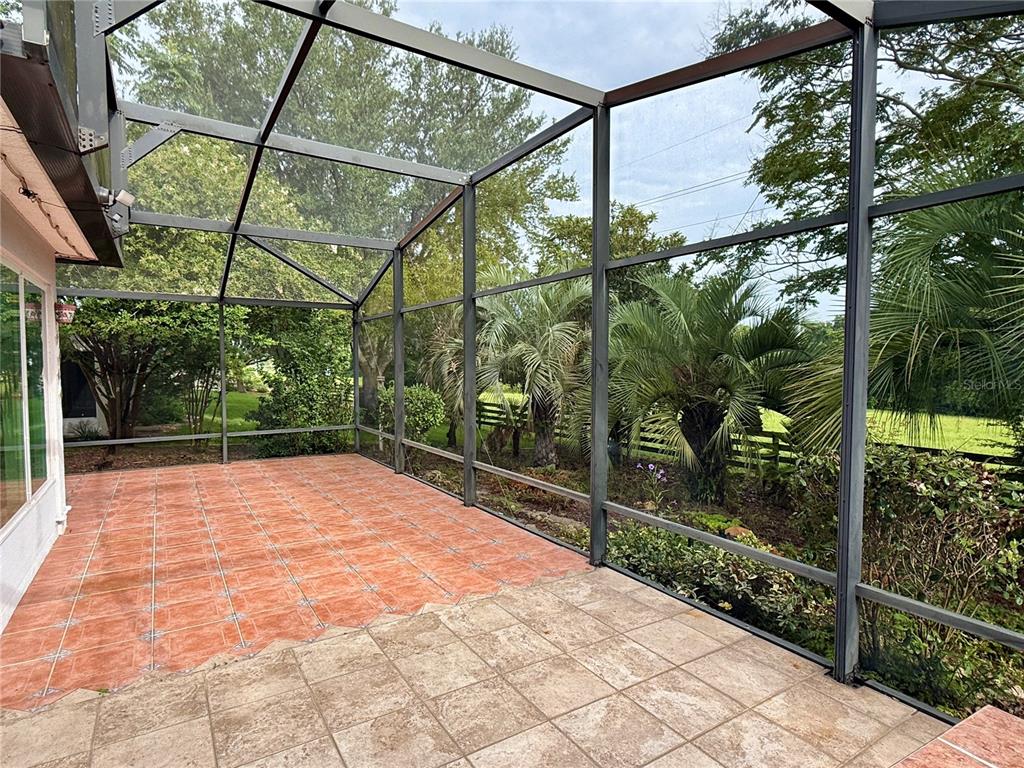 A screened-in patio features tiled flooring and views of trees and a grassy yard — 33236 GRAND CYPRESS WAY, LEESBURG, FL