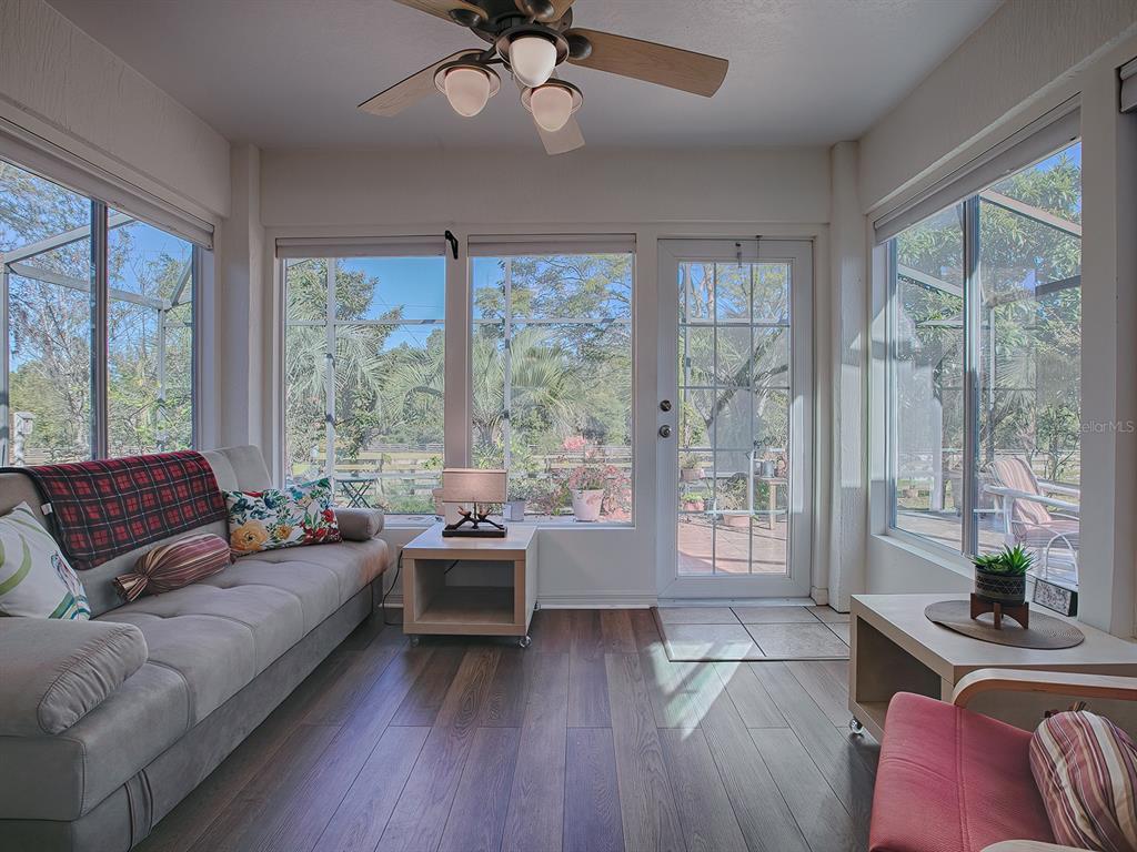 A sunroom features wood-look flooring, a ceiling fan, a sofa, and large windows overlooking greenery — 33236 GRAND CYPRESS WAY, LEESBURG, FL