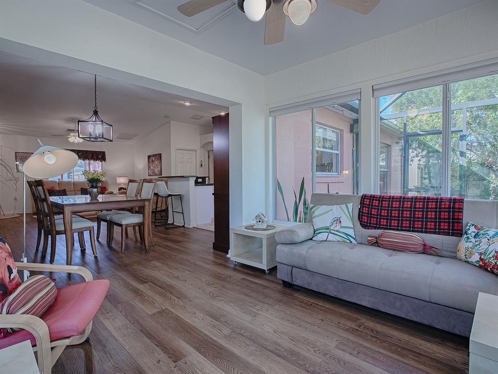 A living room with wood-look flooring, a grey sofa, and an open view into a dining area — 33236 GRAND CYPRESS WAY, LEESBURG, FL