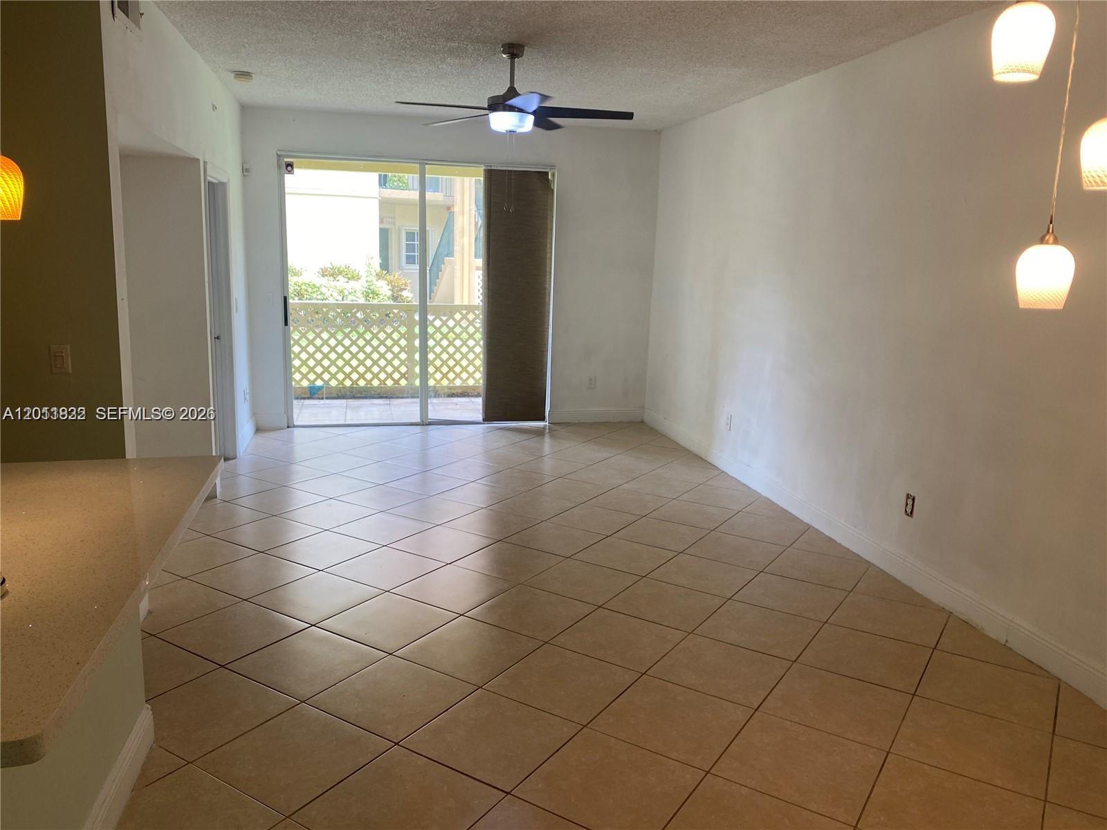 An empty living area features tile flooring, a ceiling fan, and a sliding glass door — 18330 NW 68th Ave # G, Hialeah FL 33015, HIALEAH, FL